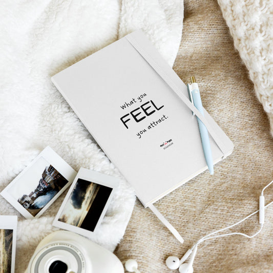Notebook with 'What you FEEL, you attract' text on a textured surface with photos and earphones.