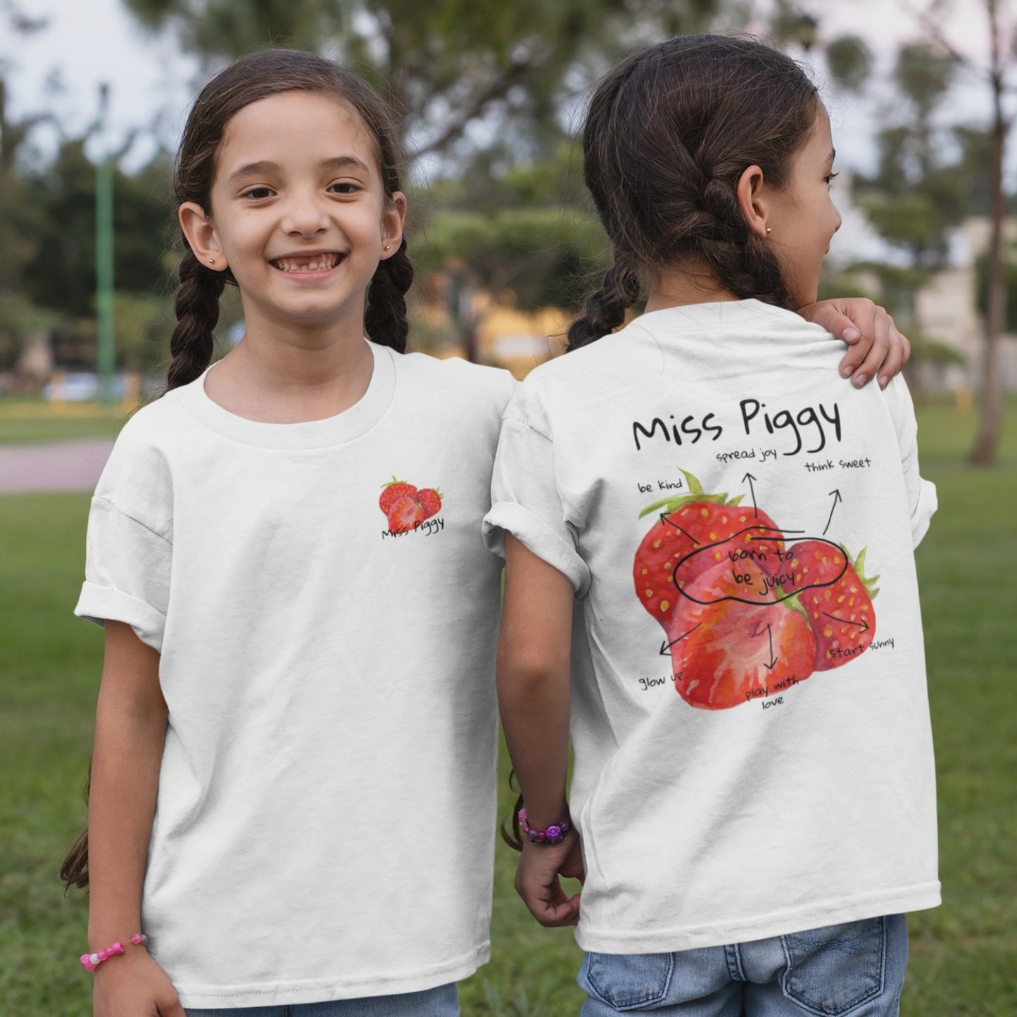 Two kids wearing the JUICY t-shirt in white. Unisex organic cotton design with soft texture and playful energy, shown in a light and joyful setting.