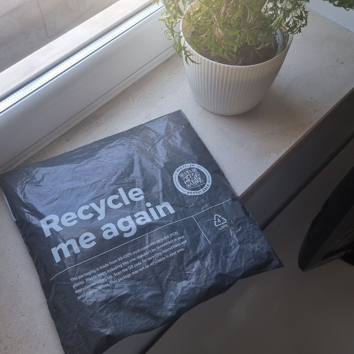 Packaging titled 'Recycle me again' on a surface with a plant in the background