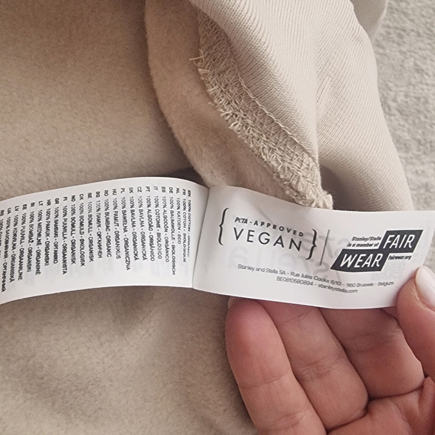 Close-up of a garment label with 'VEGAN' and 'FAIR WEAR' certification on a beige fabric background.