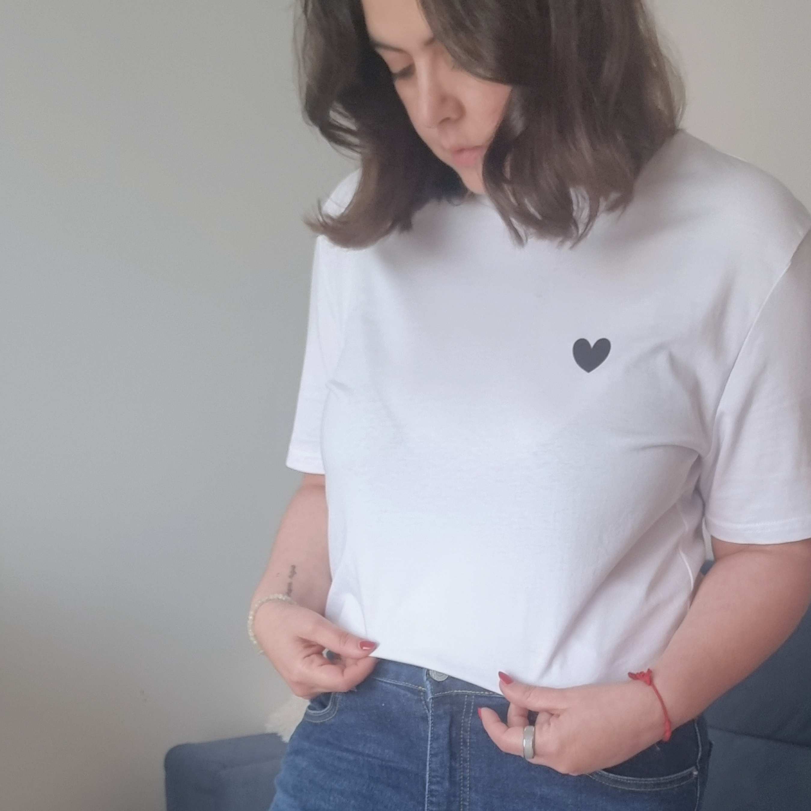 Person wearing a white t-shirt with a black heart design and blue jeans, sitting on a couch.