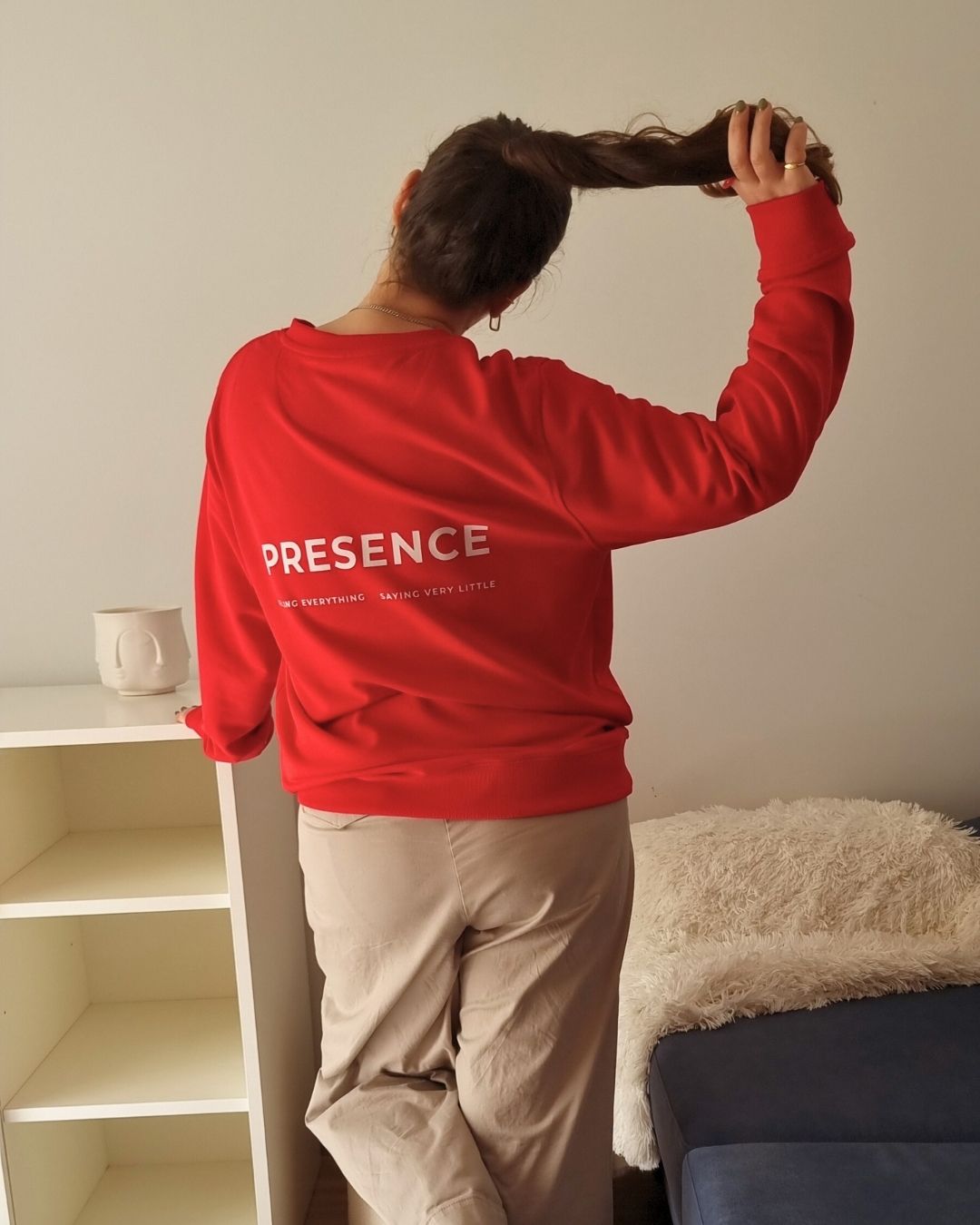 Founder wearing a red sweatshirt with 'PRESENCE' text, standing in a room.