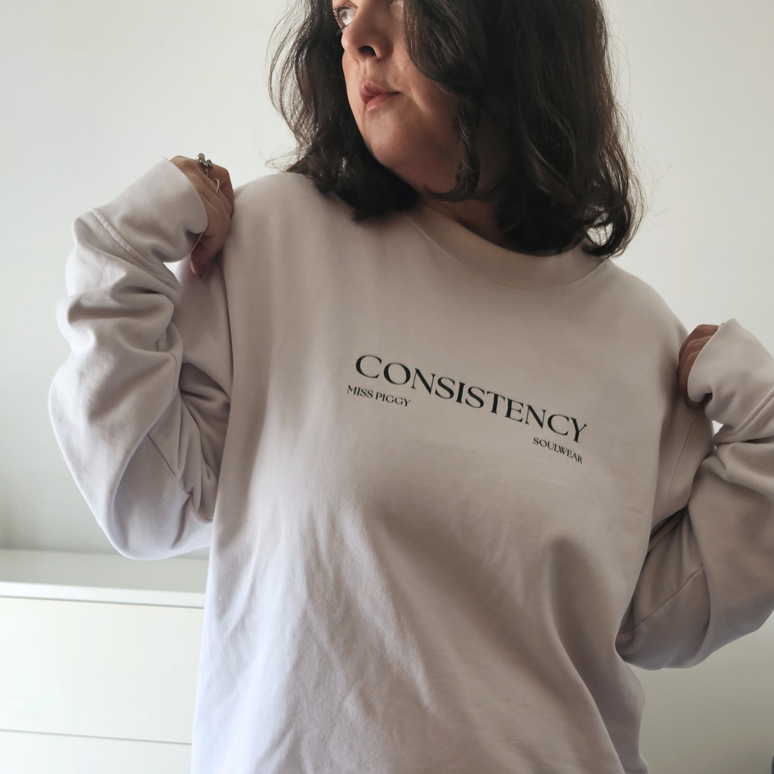 Founder wearing an organic cotton white sweatshirt with 'CONSISTENCY' text on a plain background