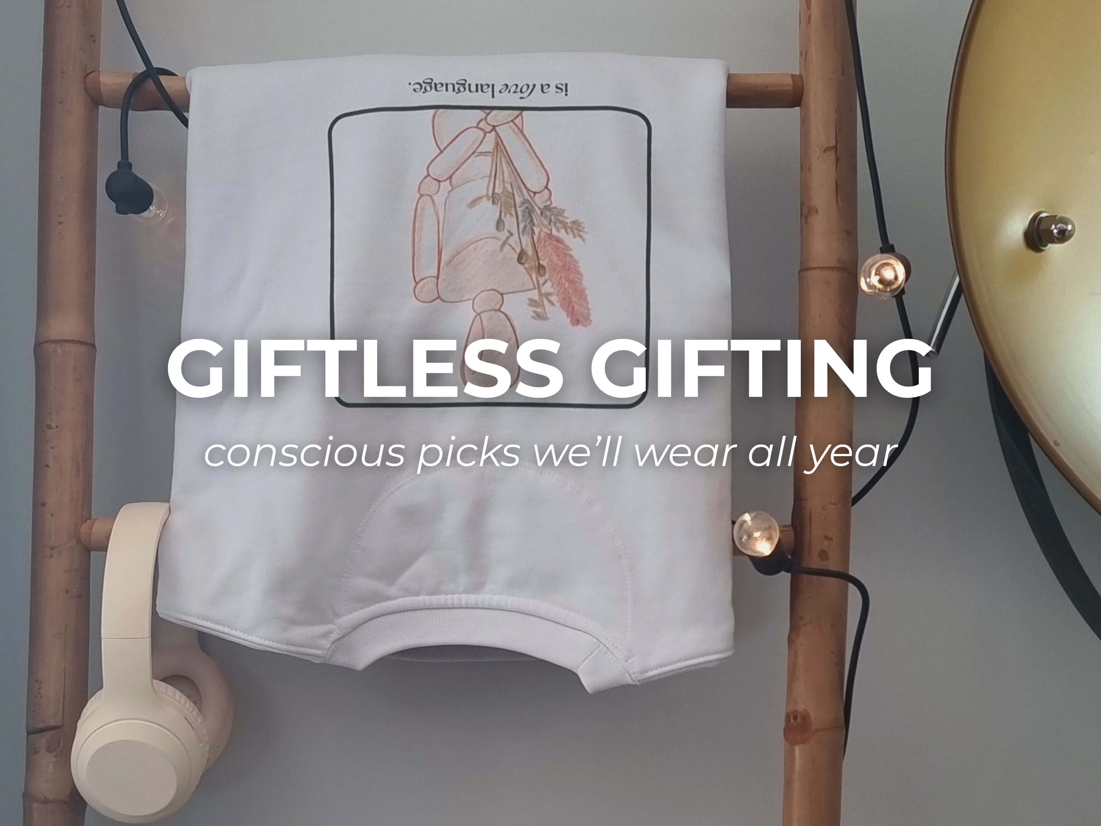 Consistency organic sweater with a design on a wooden rack, featuring text 'Giftless Gifting' and 'conscious picks we'll wear all year'.