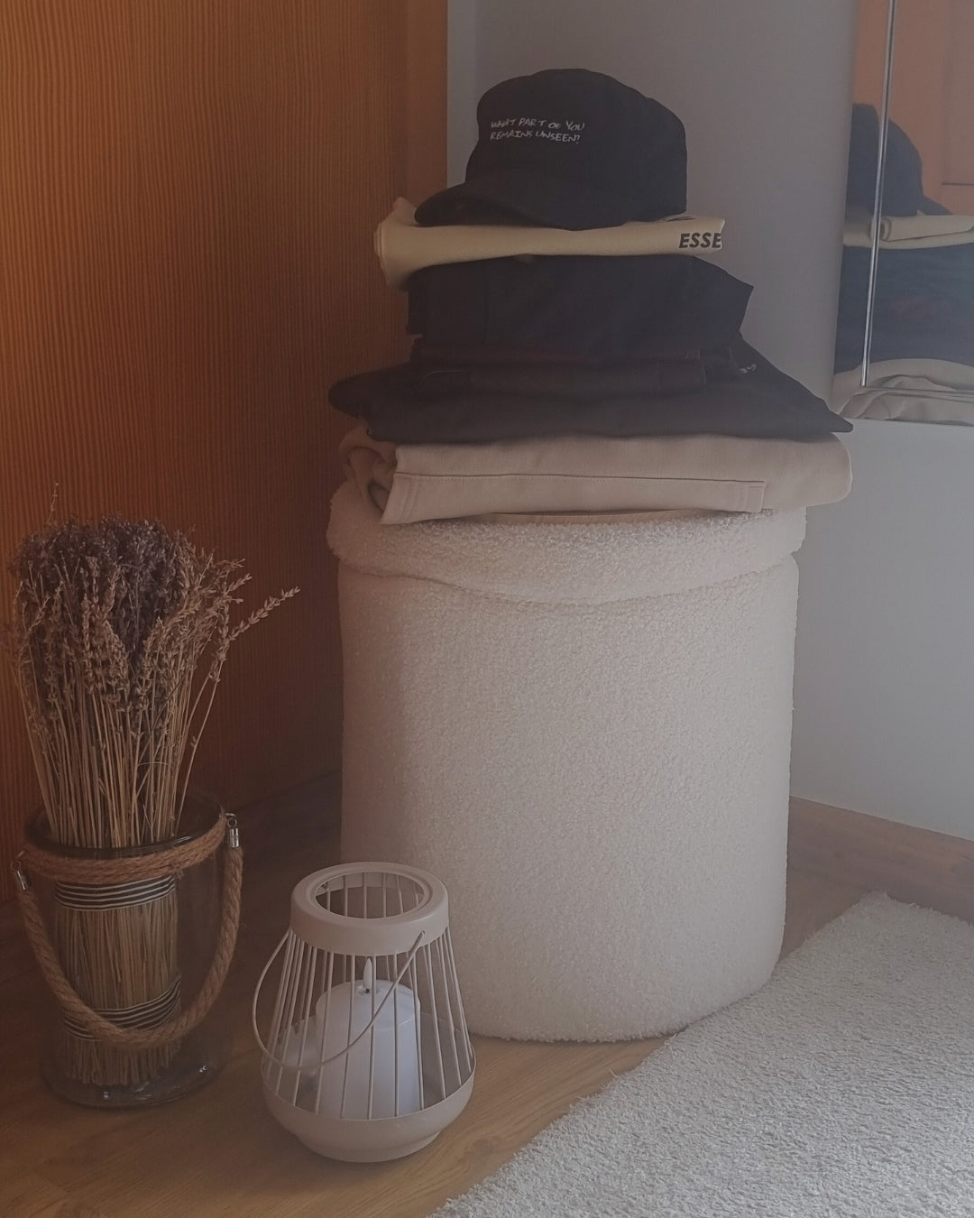 Stack of folded Miss Piggy clothes on a beige ottoman next to a lavender plant and small lantern.